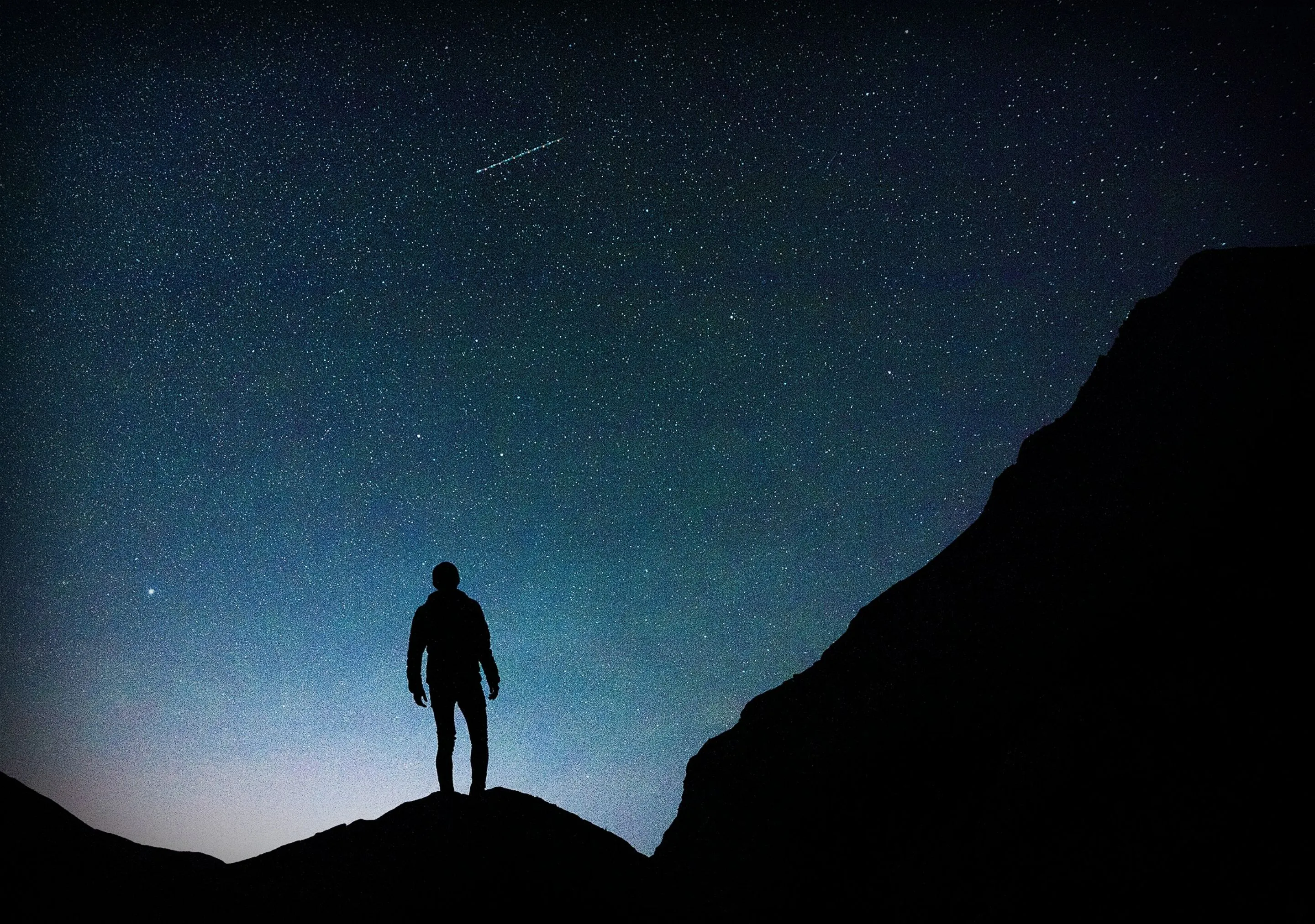 Silhouette of person on hill under starry night sky.

