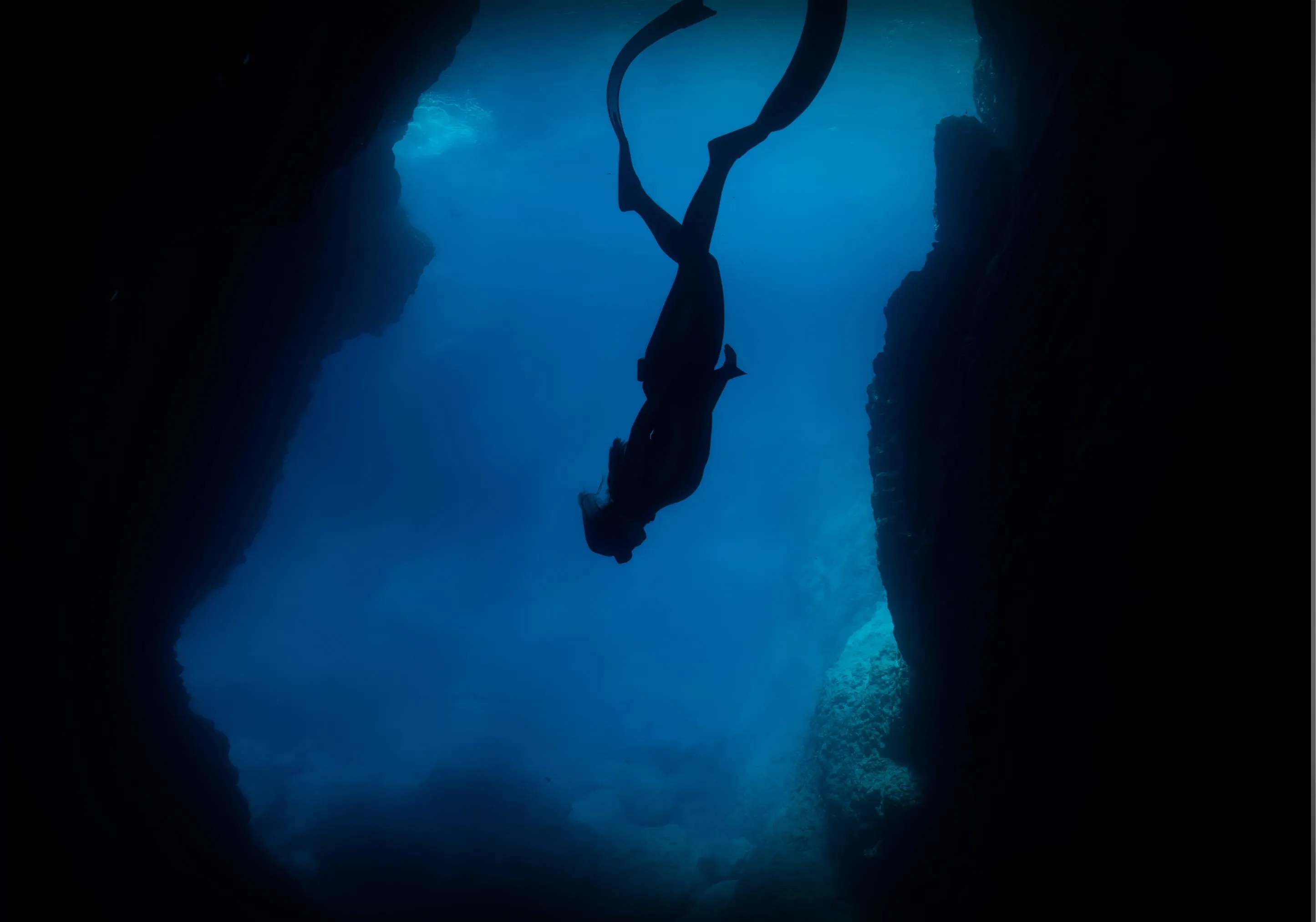 Silhouette of a diver swimming through an underwater cave.
