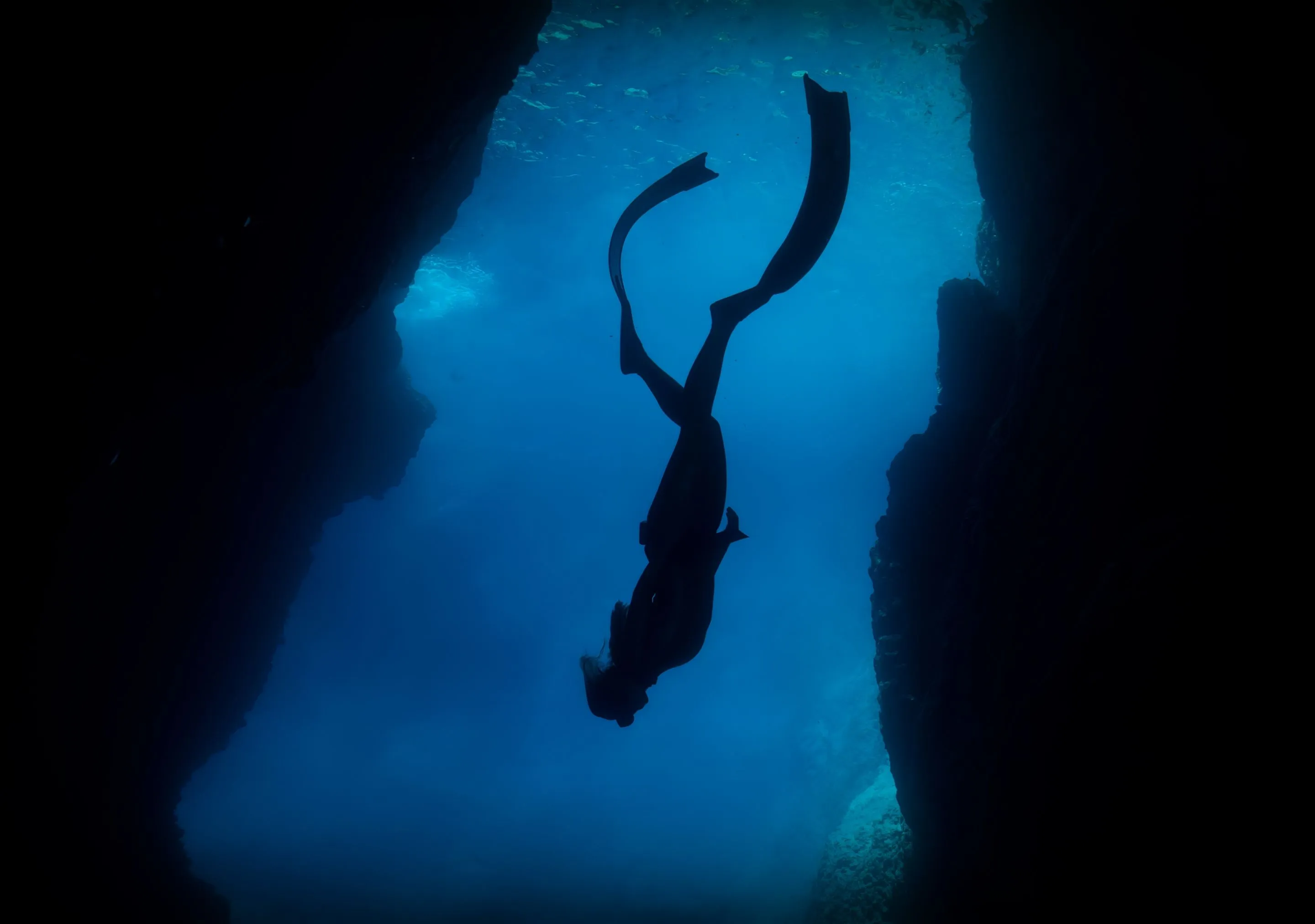 Silhouette of a diver swimming between underwater rock formations.